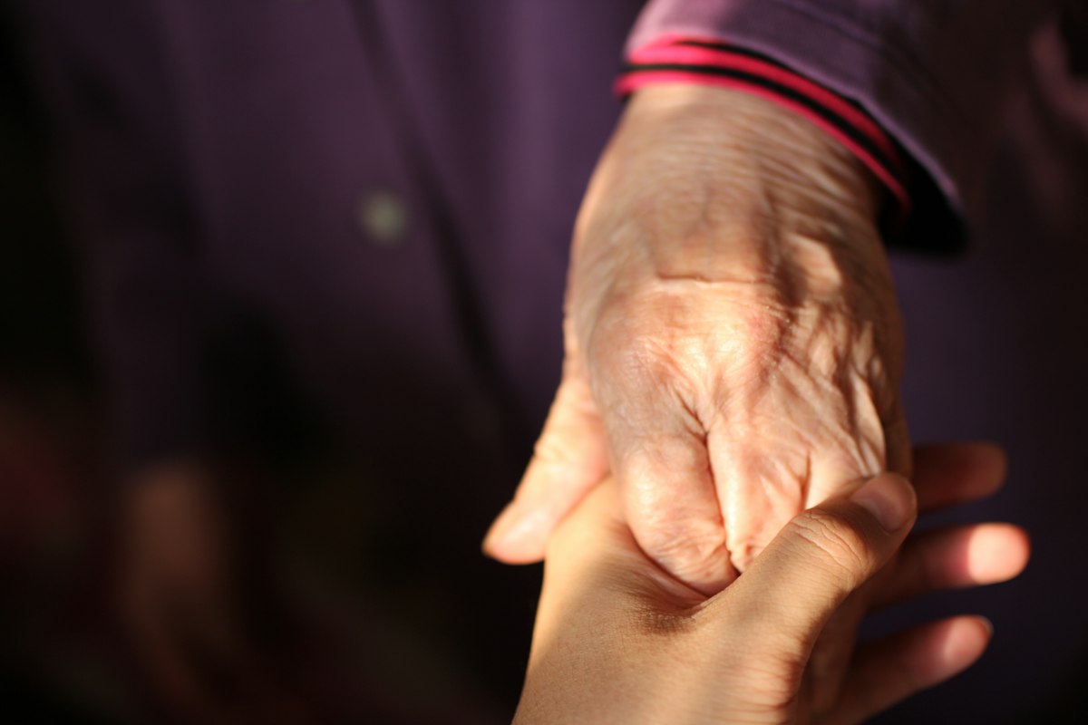 A younger hand gently holding the wrinkled hand of an older adult