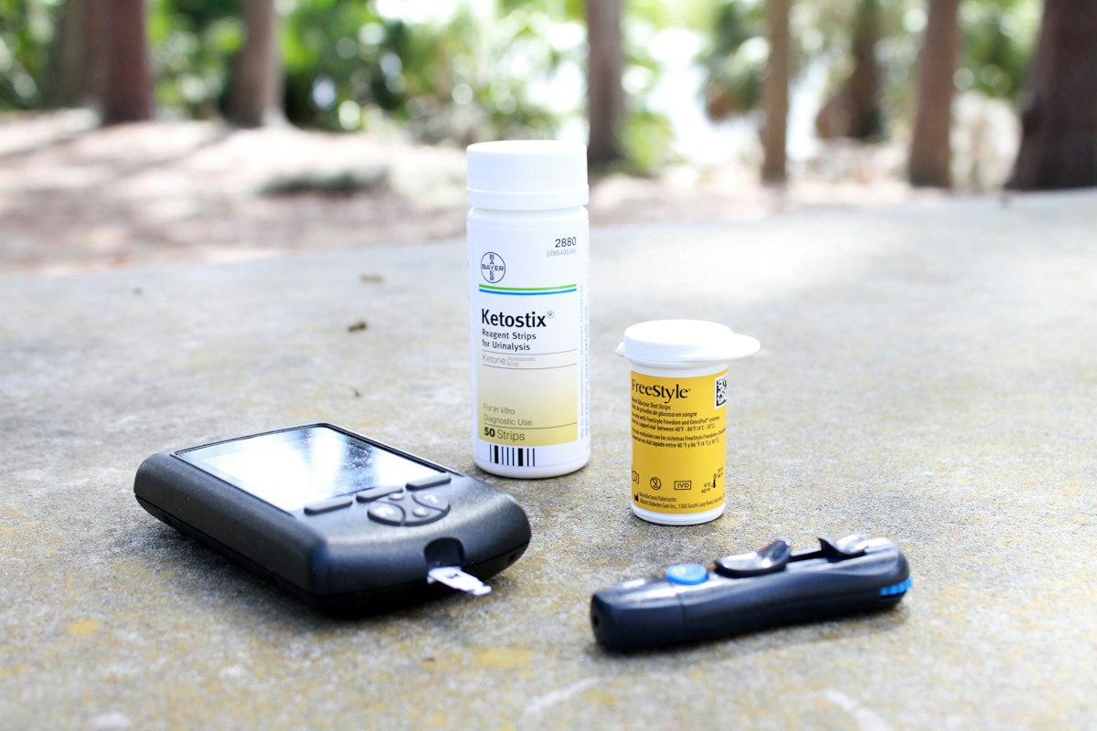 A blood glucose meter showing a reading, with test strips and a lancing device